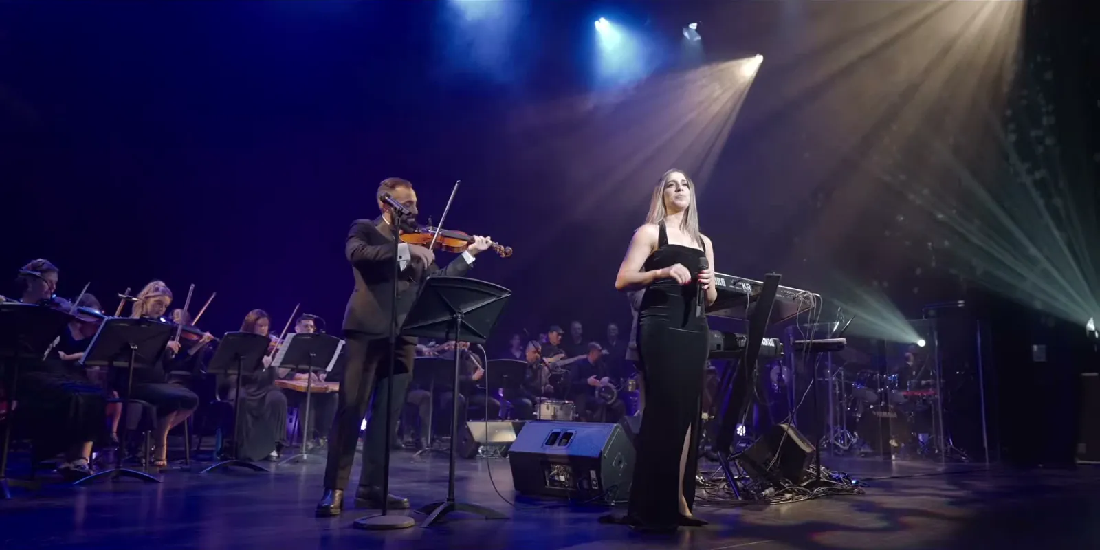 Jad on violin beside the vocalist Yara Bou Karam under stage beams