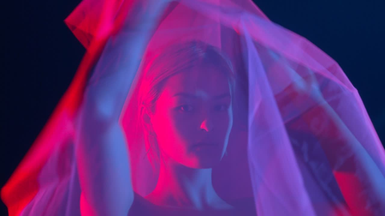 A face behind a veil, lit red and blue, from the short film Hypnotise