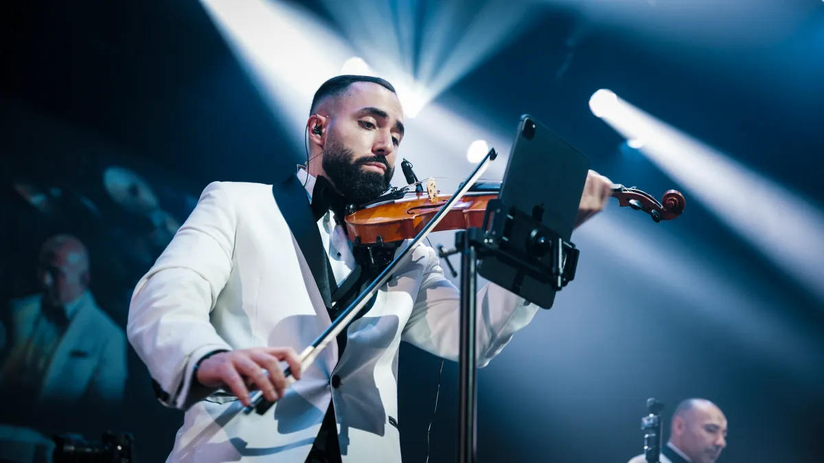 Jad playing violin in a white dinner jacket under blue stage light