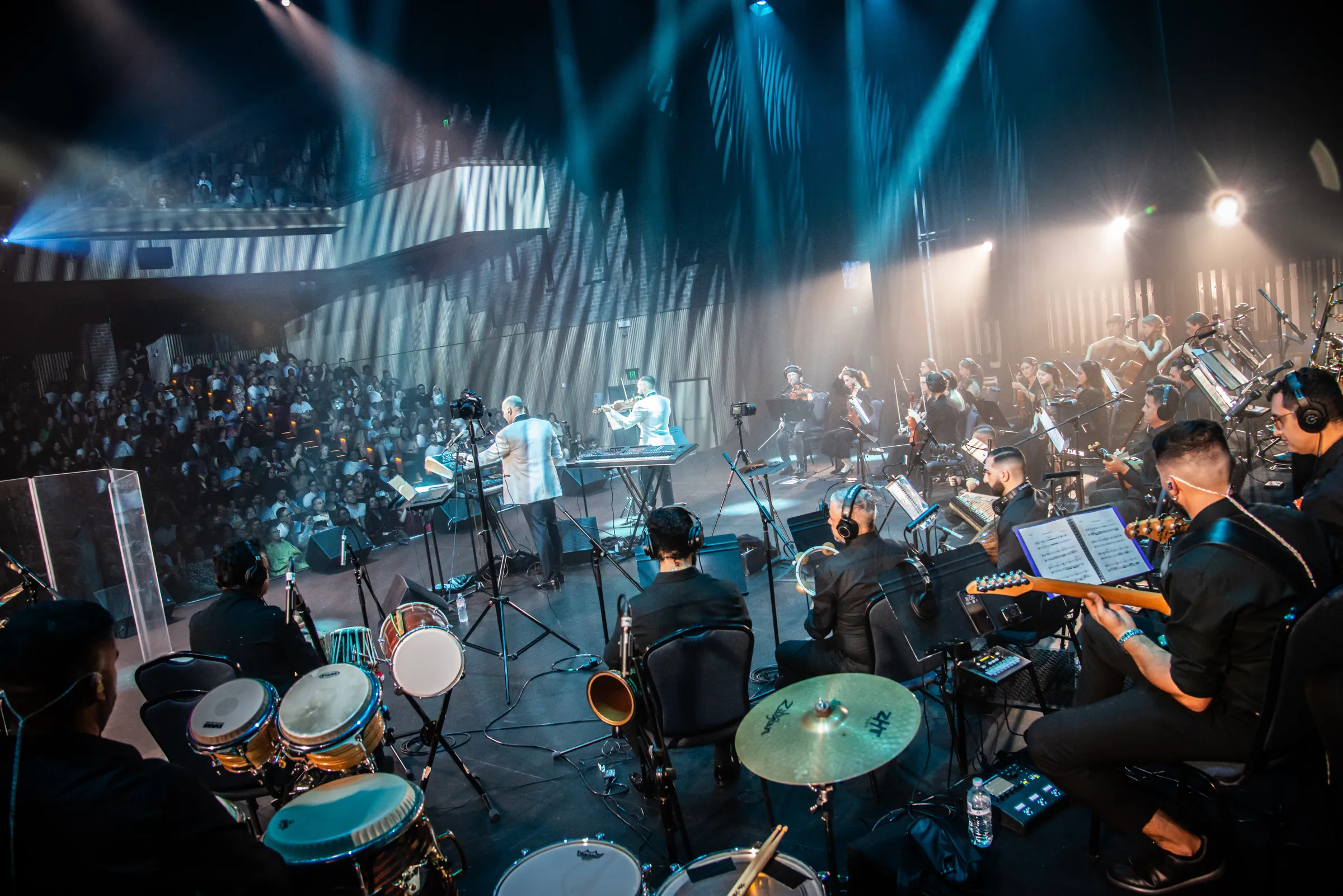 The full East–West orchestra on stage beneath a screen reading The Disaster