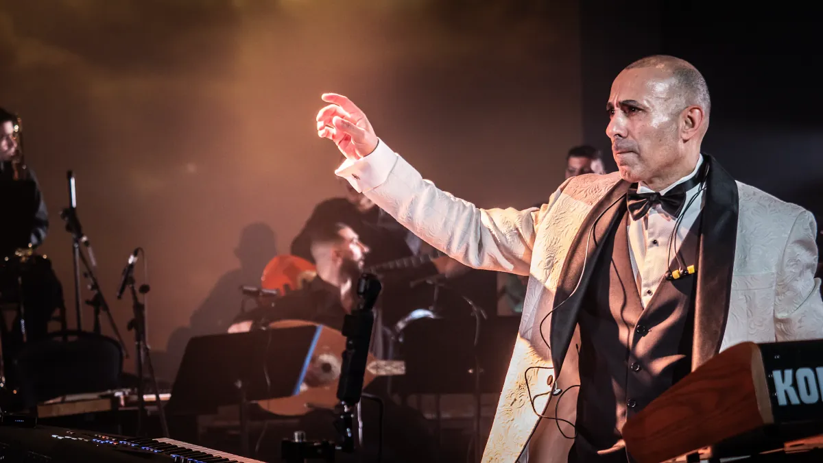 Rabih at the keys in a white dinner jacket, lit from behind