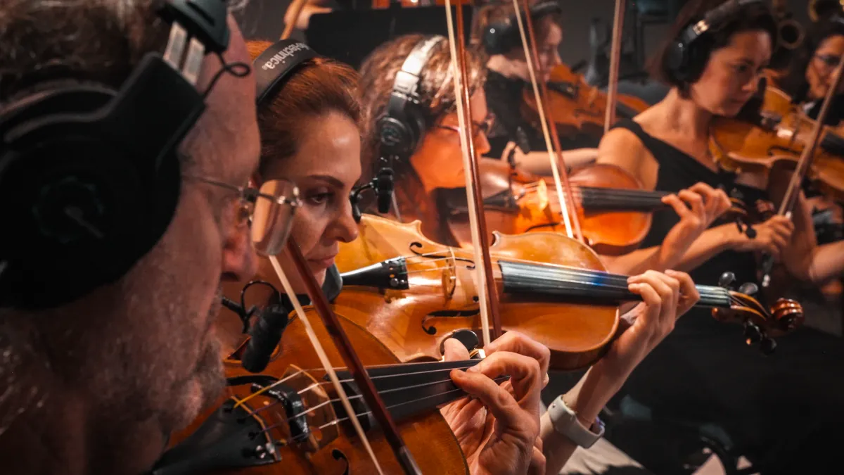 Violinists in the string section, lit in amber