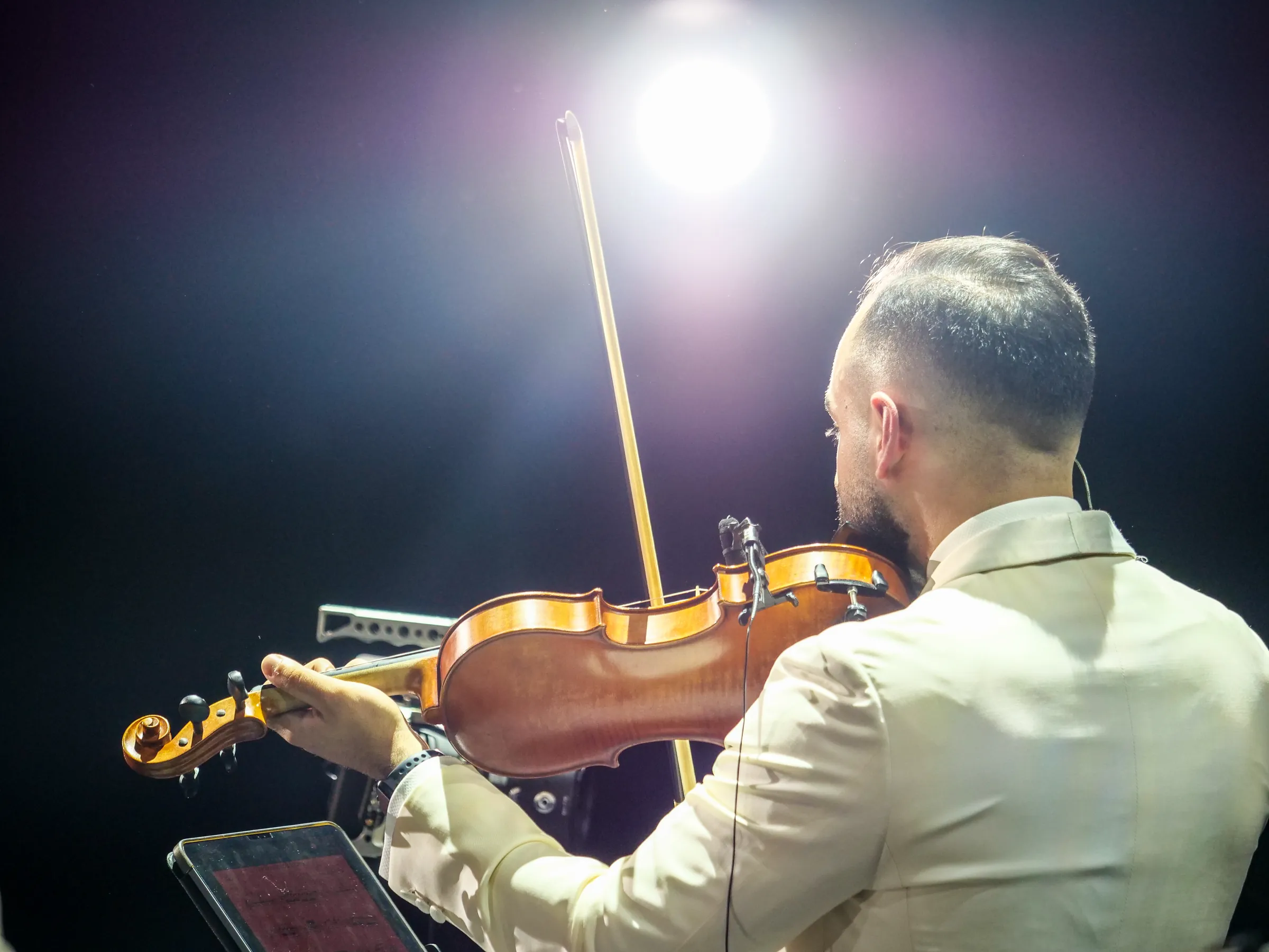 Jad playing violin under a single spotlight, seen from behind